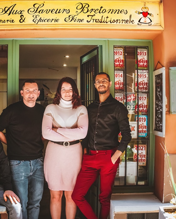 Trois personnes devant la boutique Aux Saveurs Bretonnes - Crêperie & Épicerie Fine Traditionnelle, facade verte.