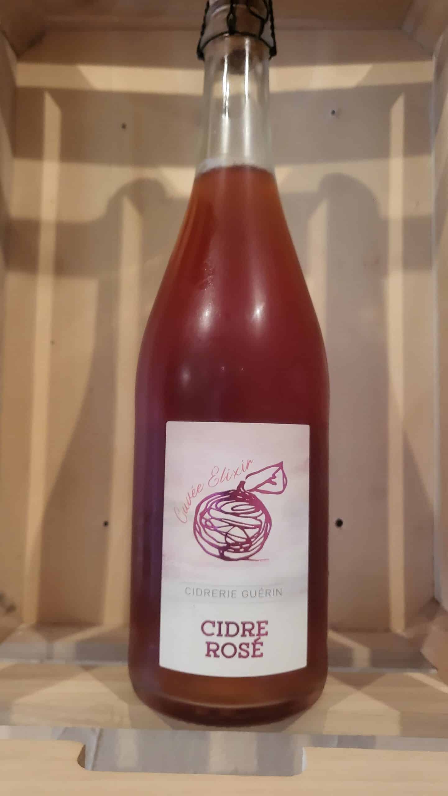 Bouteille de cidre rosé Cuvée Elixir de la Cidrerie Guérin avec une étiquette illustrée, posée dans une caisse en bois.