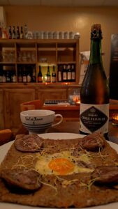 Galette bretonne à l'œuf, viande et germes, cidre fermier Kermabo et tasse Val de Rance en restaurant.