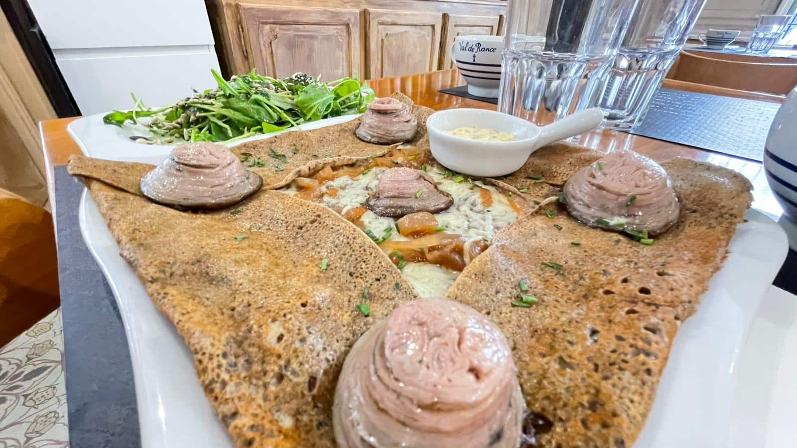 Galette de sarrasin garnie de viande, fromage fondu, oignons caramélisés, avec pâté en spirale, salade et sauce. Bol "Val de Rance".