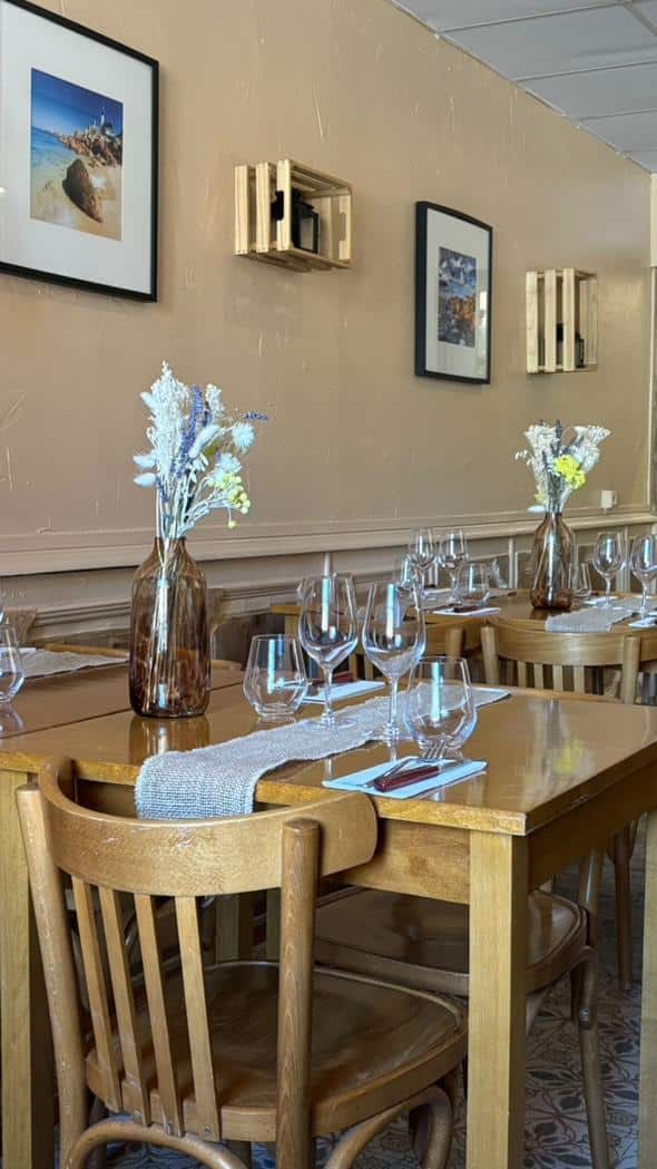 Restaurant chaleureux : tables et chaises en bois, verres, fleurs séchées. Chemins de table. Décoration murale rustique avec cadres et caisses en bois.