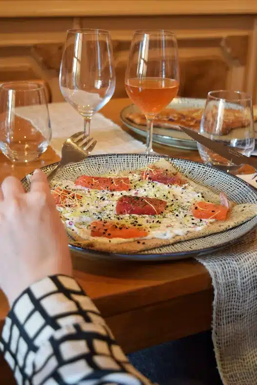 Galette au saumon fumé et crème servie dans un restaurant avec du vin rosé et des verres élégants.