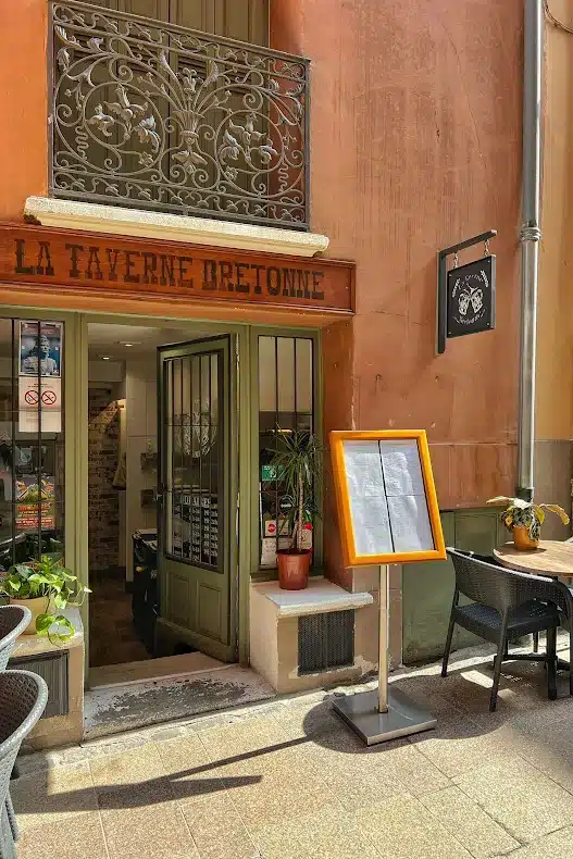 Entrée de La Taverne Bretonne avec menu extérieur, porte verte et balcon en fer forgé fleuri.