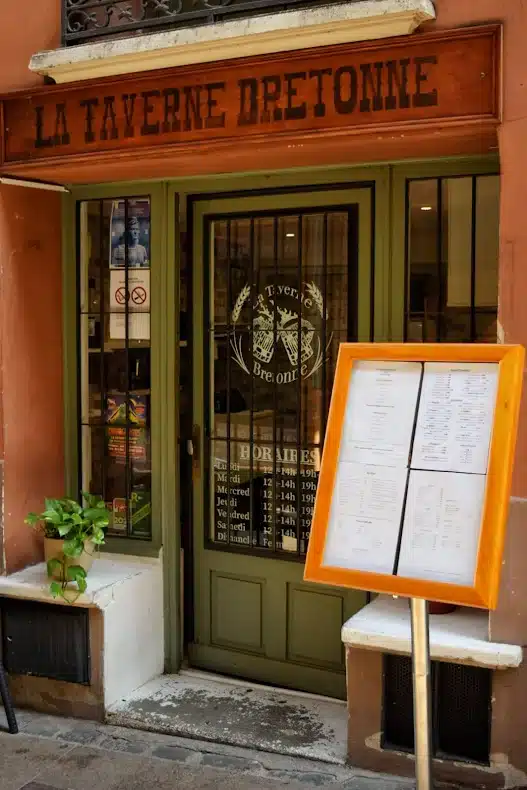 Façade de La Taverne Bretonne avec son enseigne en bois, menu extérieur et horaires sur la porte verte.