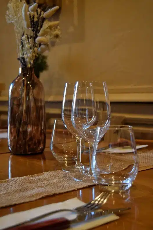 Table dressée avec verres à vin, vase de fleurs séchées et chemin de jute dans une ambiance de restaurant chaleureuse.