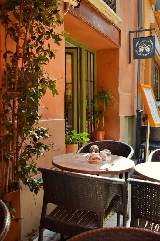 Terrasse de La Taverne Bretonne avec table dressée, chaises tressées et plantes devant une façade orange ensoleillée.